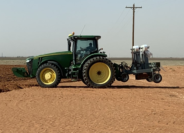 Alpha subsurface water retention membrane prototype pulled behind a John Deere tractor in a sandy field in Yoakum County, Texas
